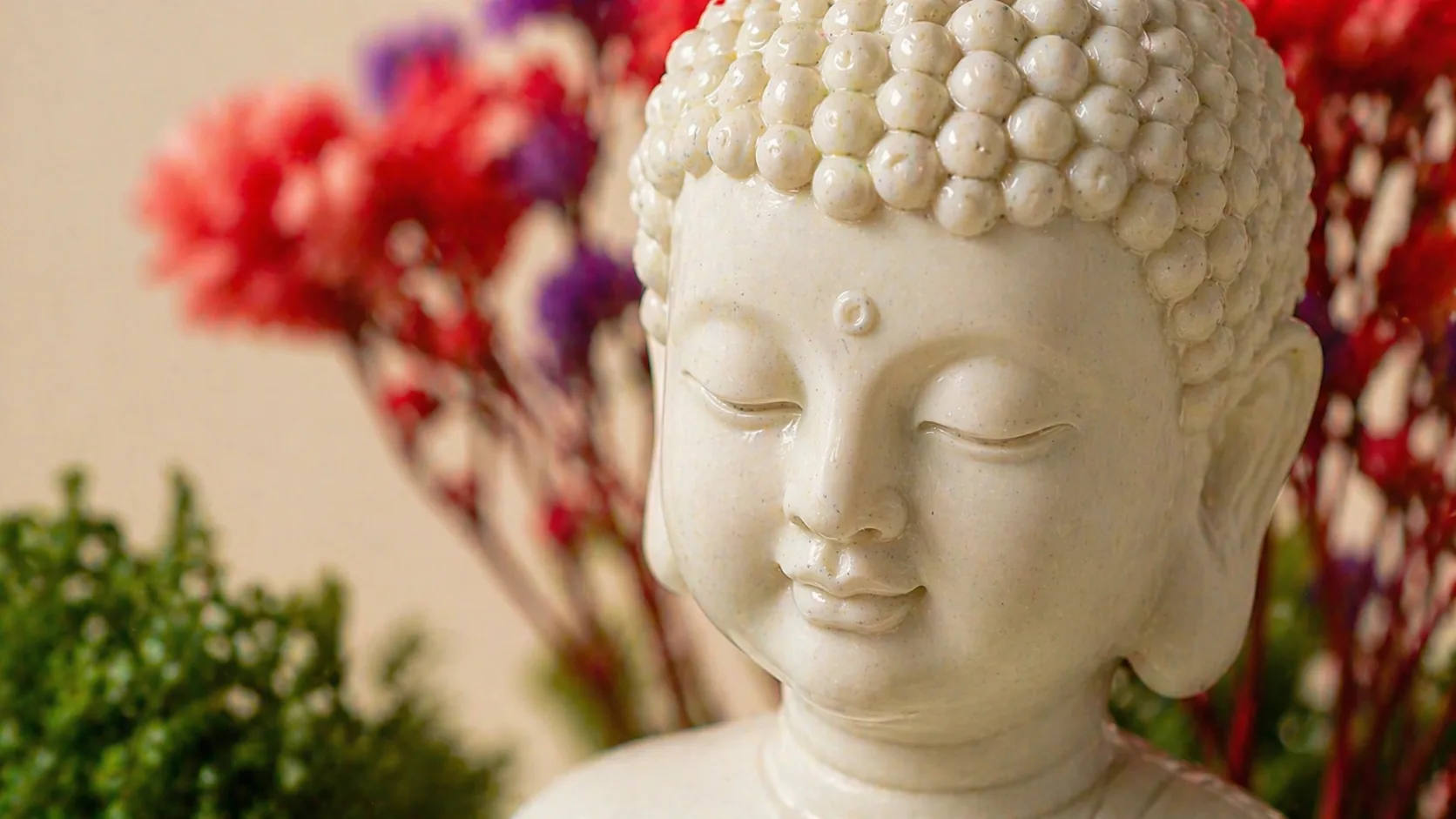 Close-up of the resin Buddha's calm face against red and purple preserved flowers. A digitally styled view made from our product photograph.