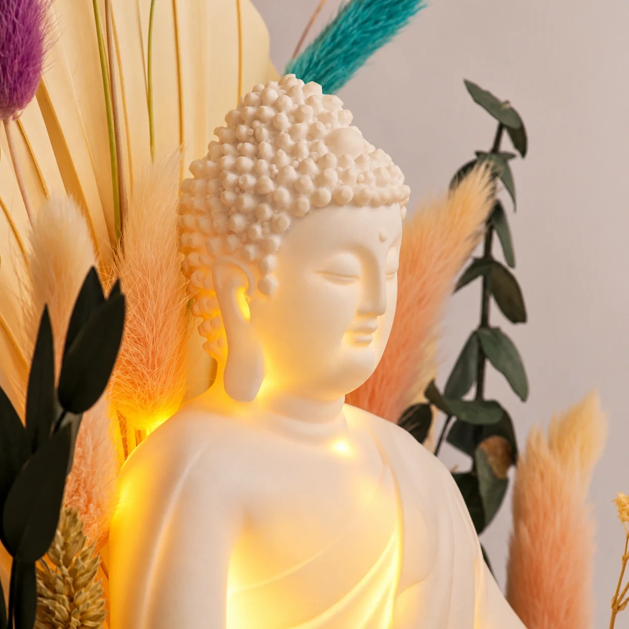Close-up of the white Buddha's face, glowing, among dried grasses and leaves