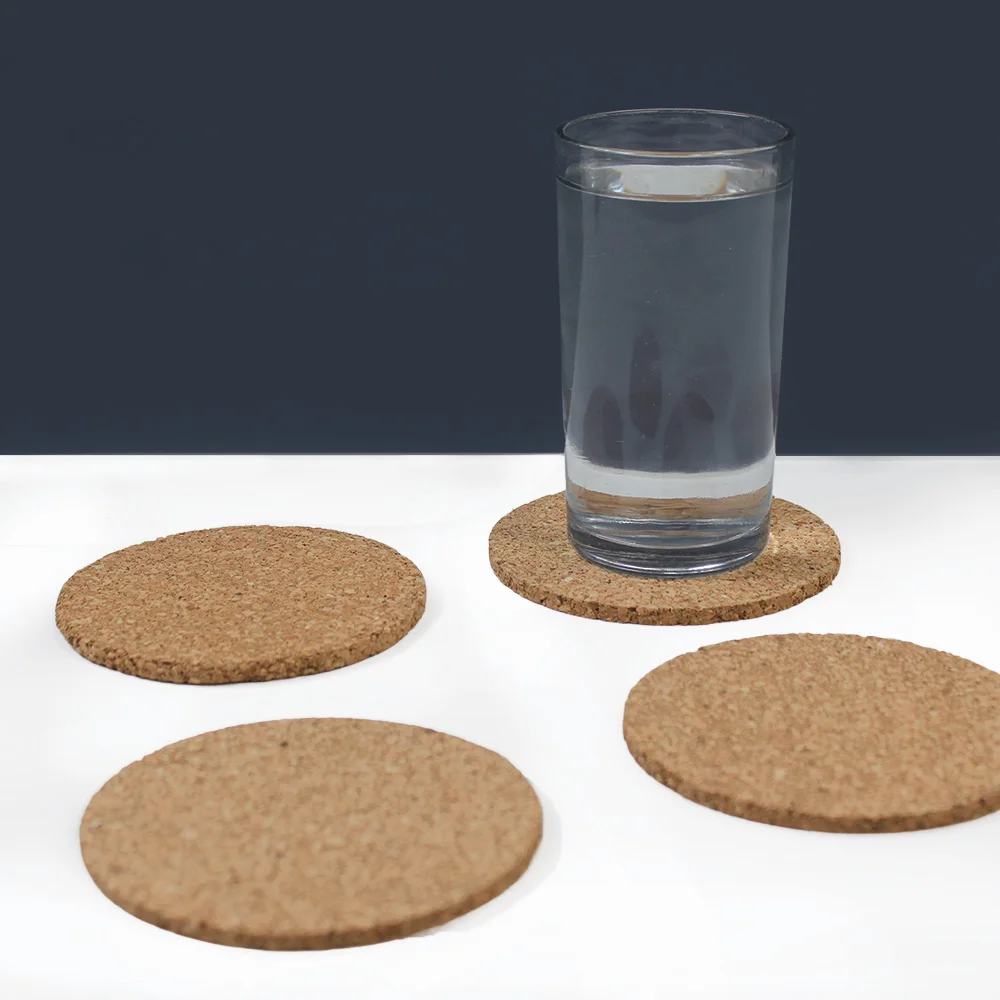 Four plain round cork coasters on a table, one under a glass