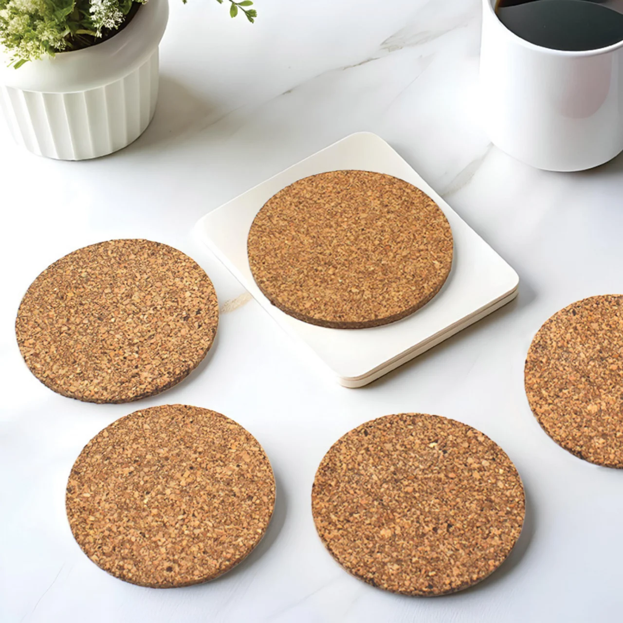 Round cork coasters on a table beside a cup and a small plant