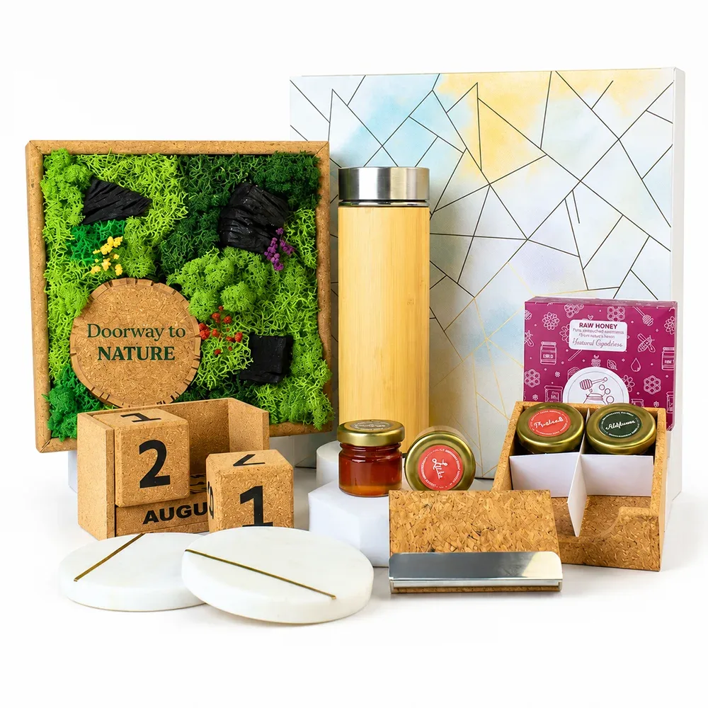 The Forest Chronicles Box laid out: a 9-inch moss frame with a cork circle, a bamboo flask, a tray of four honey jars with their pink box, a cork block calendar, a cork card holder and two marble coasters, in front of the watercolour gift box