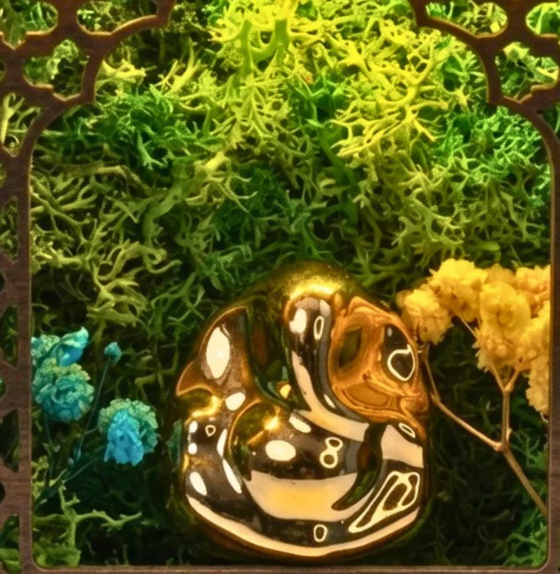 Close-up of the golden ceramic Ganesha among preserved moss with small flowers
