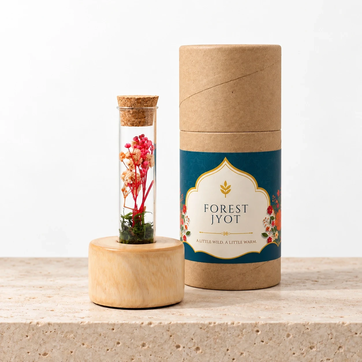 Forest Stump Tall Festive: a cork-stoppered glass bottle of pink and peach preserved flowers on a wooden stump beside its Forest Jyot paper tube, on a limestone shelf in soft window light