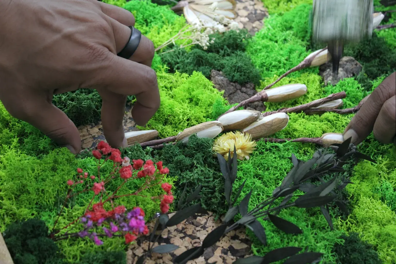 Hands setting dried flowers and stems into a bed of preserved moss, in our workshop