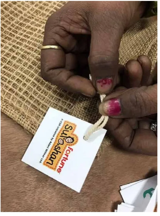 A hand tying a printed tag onto a jute bag