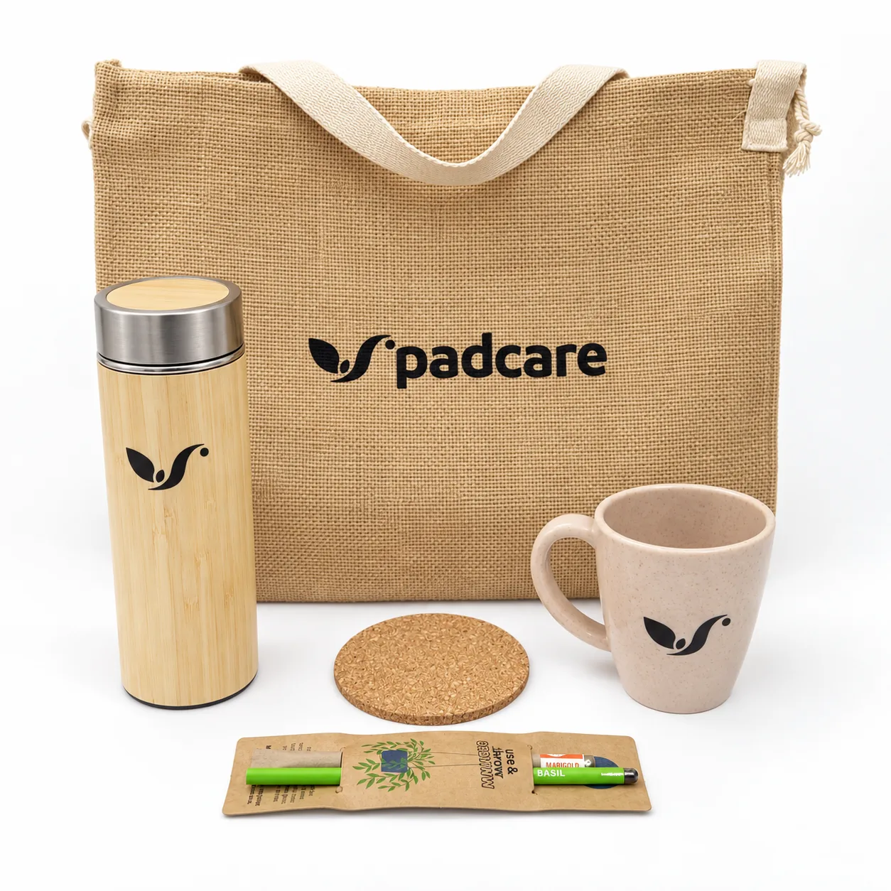 A jute tote printed padcare, a bamboo flask, a coffee-husk mug, a cork coaster and two plantable paper pens on a kraft card, all with the mark