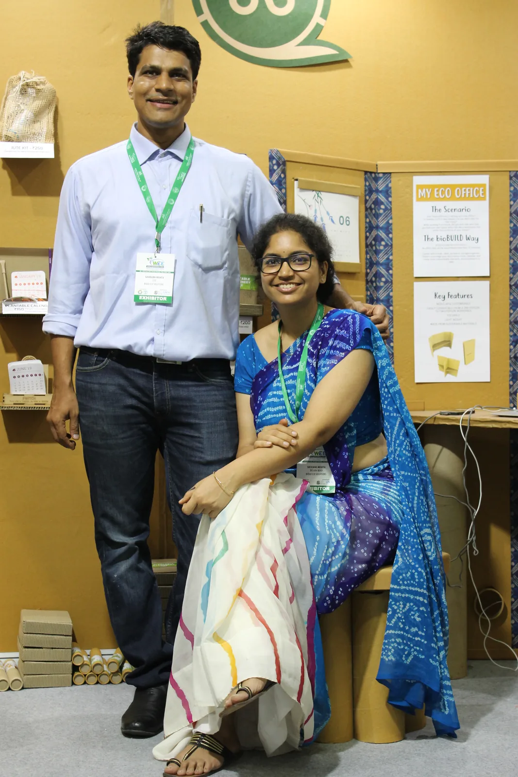 A man standing and a woman seated on a cardboard stool in front of the stall wall