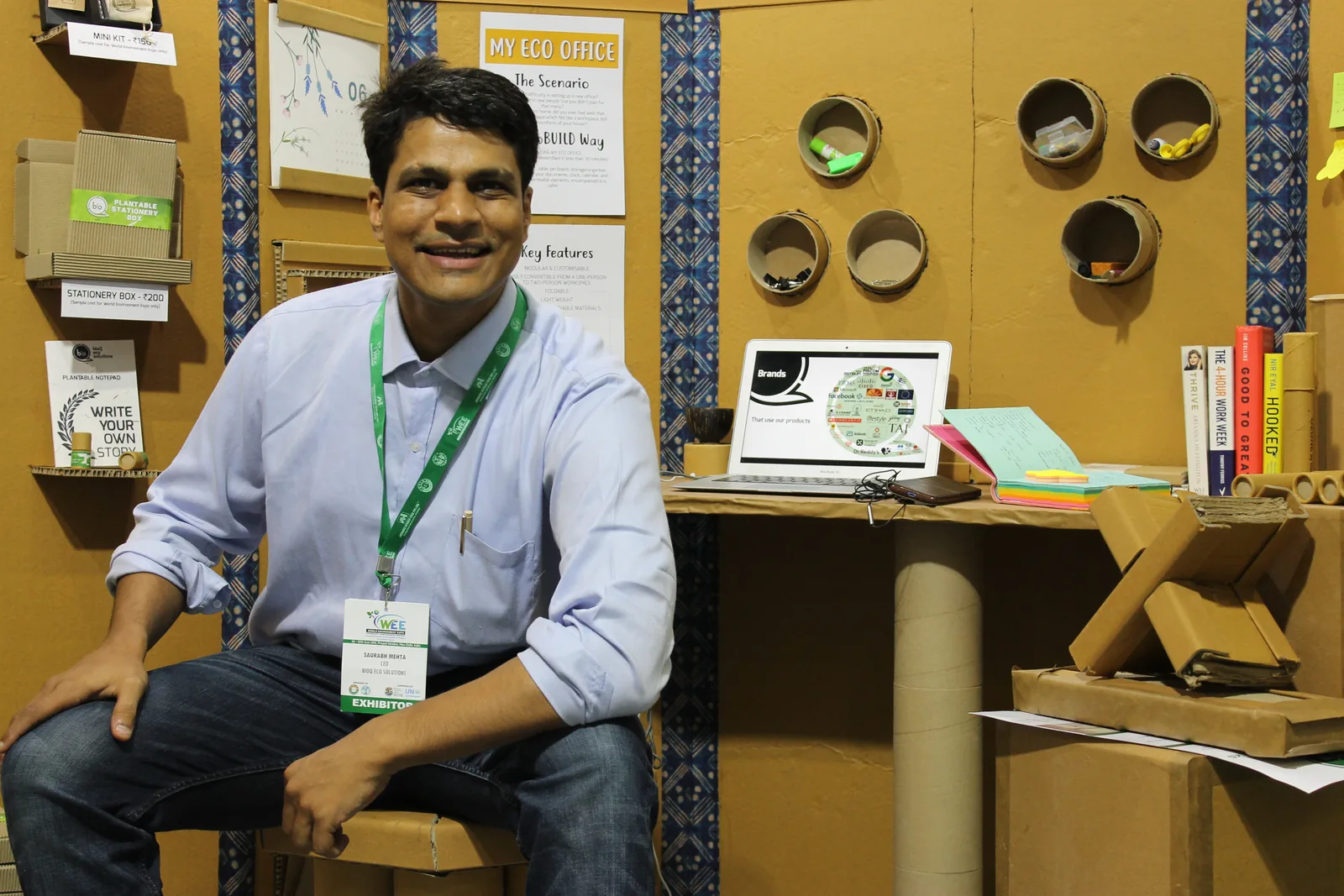A team member smiling at a cardboard desk with a laptop and books