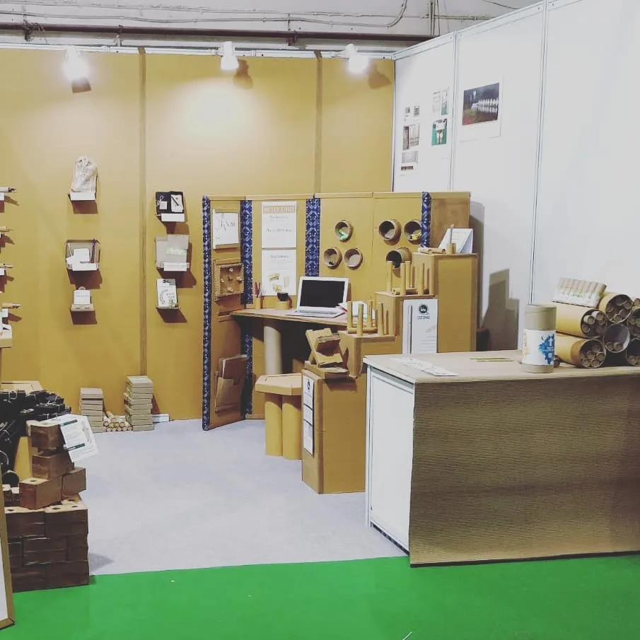The stall on a green carpet: cardboard walls, desks and tubes under the show lights