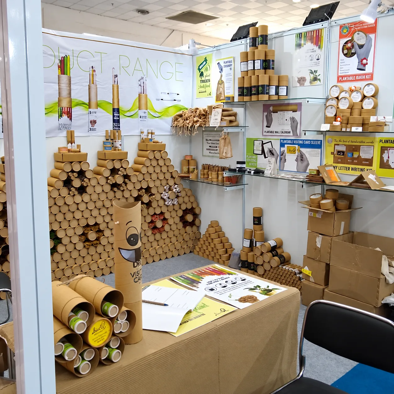 A stall with a table and a wall built from stacked paper tubes with flowers set in them