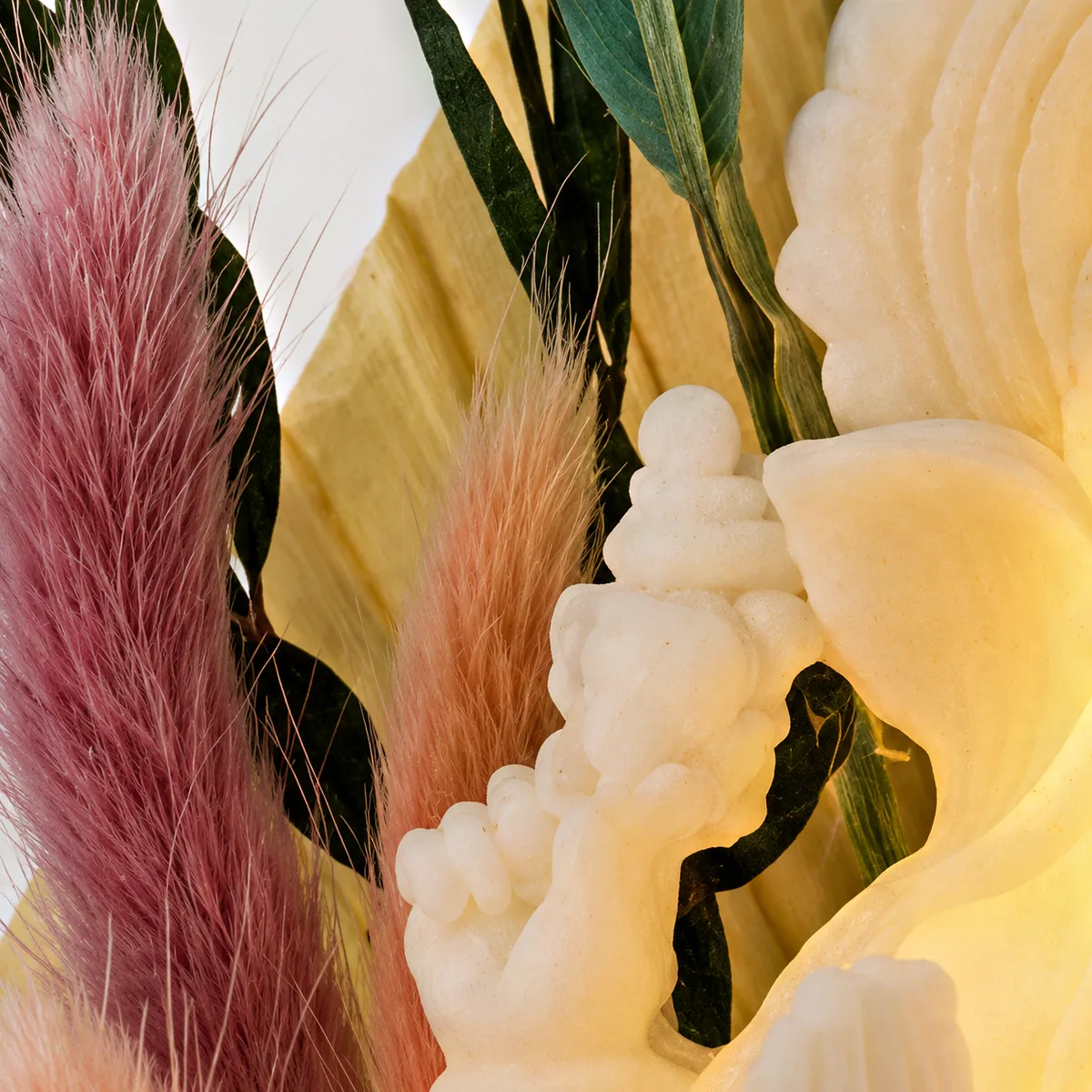 Close-up of pink and green preserved grasses and leaves beside the white Ganesha