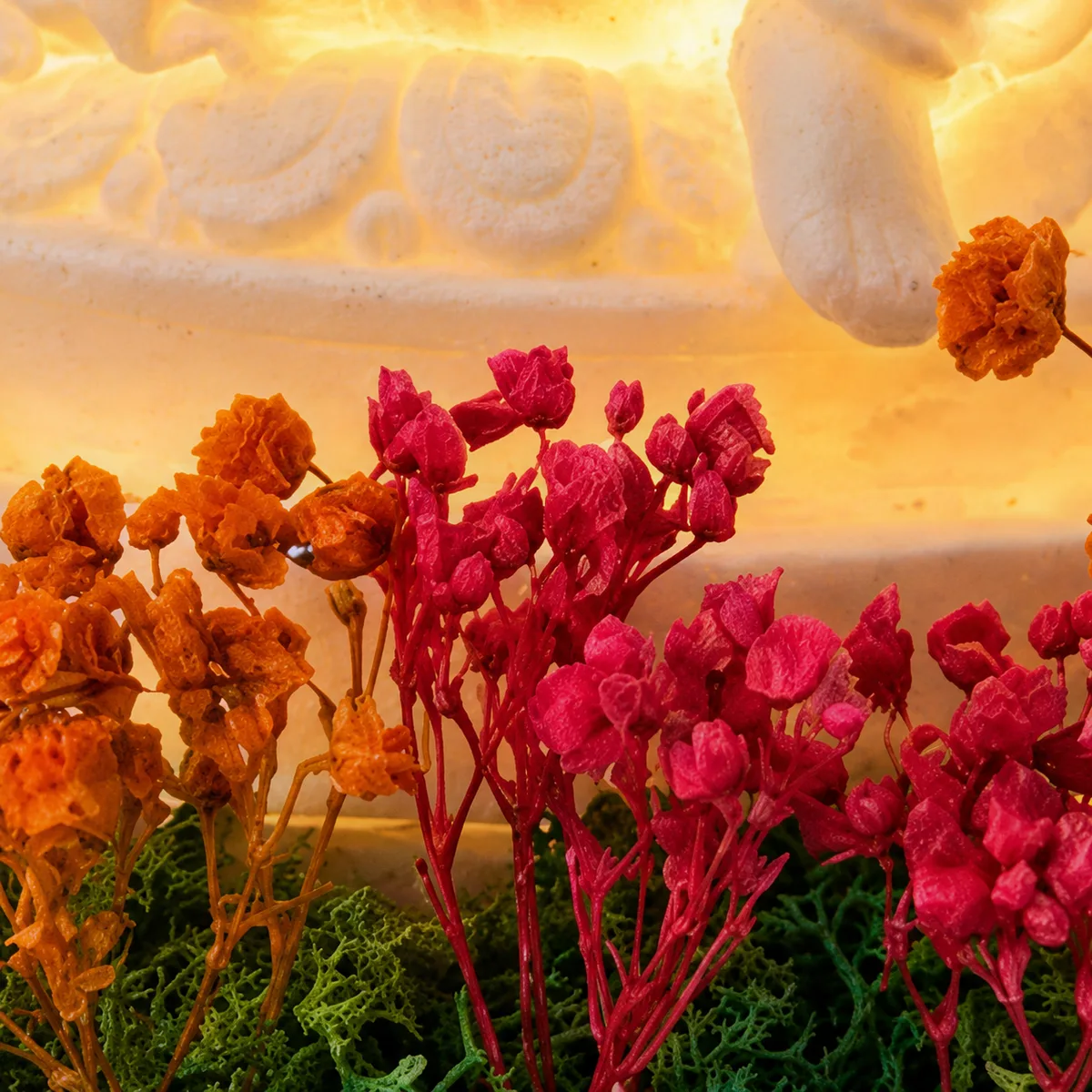 Close-up of small red and orange preserved flowers on moss in front of the lit Ganesha